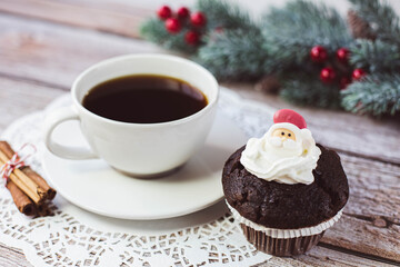 Chocolate muffin with decorative santa claus, white cup with black coffee and other christmas...