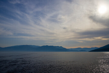 Nature scenery landscape of sea surrounded by mountain and sun and clouds on horizon background