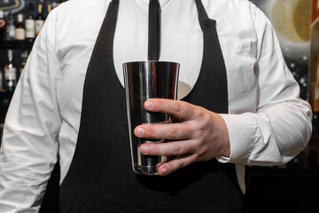 The hand of a professional bartender man holds a tool for mixing and making shaker cocktails