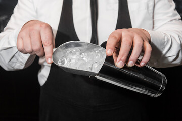 The hands of a professional bartender add ice in a scaple to a tool for preparing and mixing...