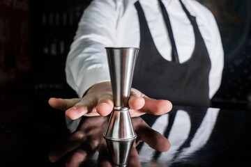 The hand of a professional bartender holds a jigger tool or measuring cup to control the...