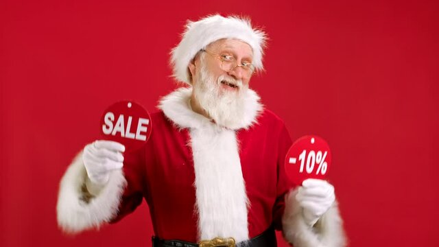 Christmas SALE -10 Off. Cheerful Santa Claus is Dancing and Joyful From Christmas Sale Holding Two Banners With Inscription SALE and -10 Off Showing Off Inscriptions to Camera on Red Background.
