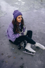 A beautiful woman is sitting on a skating rink and holding a thermos of hot tea in her hands. Toned in trendy Very Peri color of the Year 2022