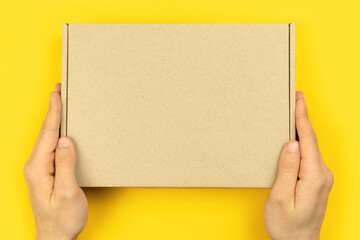 Delivery man hands with cardboard box mockup, top view. Yellow table background. Shipping and delivery concept, copy space photo