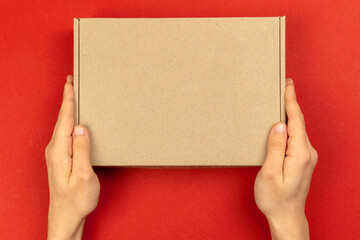 Delivery man hands with cardboard box mockup, top view. Christmas gifts concept. Red table background. Shipping and delivery, copy space photo