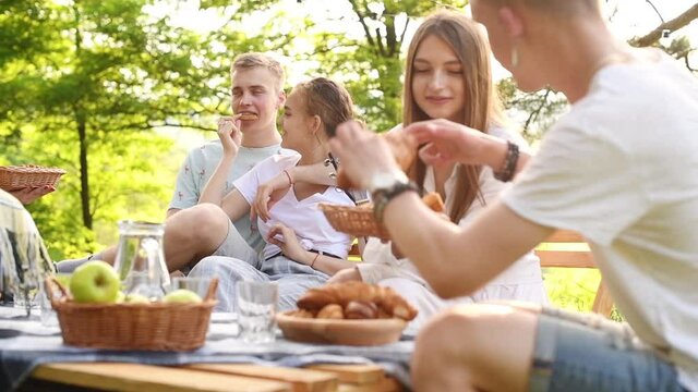 Eating and talking. Young cheerful people in casual clothes have a picnic outdoors in the forest