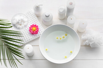Spa set with bowl of water on light wooden background