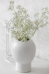Vase with gypsophila flowers on table near light wall