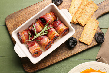 Baking dish with prunes baked in crispy bacon on color wooden table