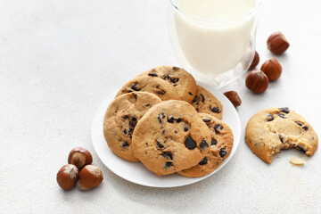 Plate with tasty homemade cookies, glass of milk and chestnuts on light background