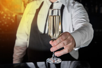 A professional bartender serves chilled champagne sparkling with gases in glass on the bar