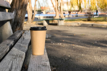 Naklejka premium Takeaway cup of tasty latte on bench in park