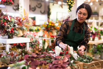 Focused asian woman seller working in a store decorates a Christmas composition with candles