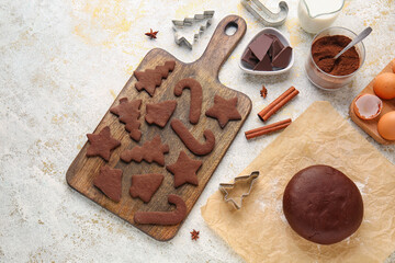 Wooden board with tasty chocolate Christmas cookies and dough on light background
