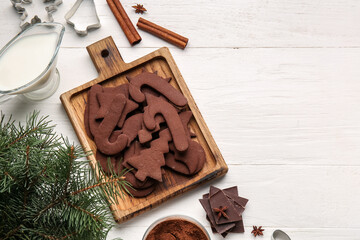 Board with tasty chocolate Christmas cookies and ingredients on white wooden background
