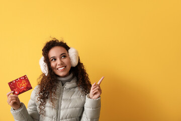 Young African-American woman with gift card pointing at something on color background