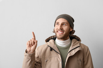 Handsome young man in winter clothes pointing at something on light background