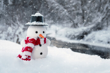 Amusing snowman stands in a snowdrift with winter river and forest on the background at countryside in cold snowy day