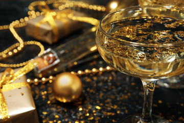 Glass of champagne and golden confetti on dark background, closeup