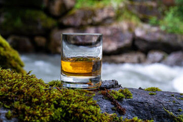 Glass of strong scotch single malt whisky with fast flowing mountain river on background