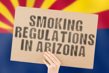 The phrase " Smoking Regulations in Arizona " on a banner in men's hand with blurred Arizona flag on the background. Judicial. Outside. Place. Pollution. Unlawful. Denial. Denied