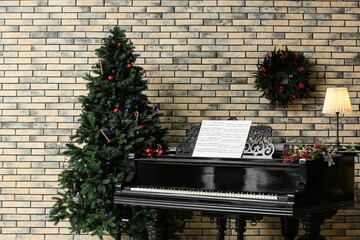 Beautiful grand piano with note sheets and Christmas tree near brick wall