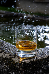 Glass of strong scotch single malt whisky served on old stone reservoir for water from mountain spring