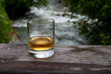 Glass of strong scotch single malt whisky with fast flowing mountain river on background