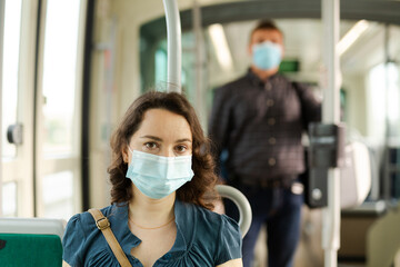 Fototapeta na wymiar Young woman wearing medical face mask sitting in modern streetcar in sunny spring day during COVID-19 virus pandemic