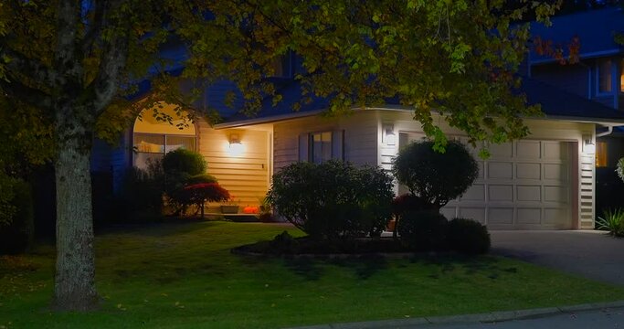 Establishing shot of two story stucco luxury house with garage door, big tree and nice landscape at night in Vancouver, Canada, North America. Night time on September 2021. ProRes 422 HQ.