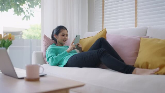 Zoom in asia young people generation z student casual teen girl enjoy fun look humor funny movie on TV app sit lying read text on cozy sofa play video live tiktok reel story with smile joy face.