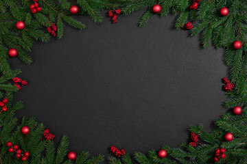 Fototapeta na wymiar Christmas frame with fir branches and red berries, baubles on a black background. Xmas greeting card. Happy New Year. Copy space, top view, flat lay.