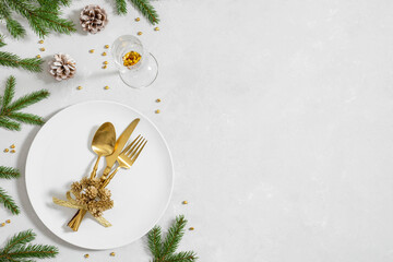 Christmas table setting with golden cutlery and fir branches on a gray background. View from above. Space for text.