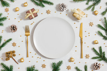 Christmas table setting with empty plate, fir branches and golden festive decorations on a gray background. Space for text. Top view, flat lay.