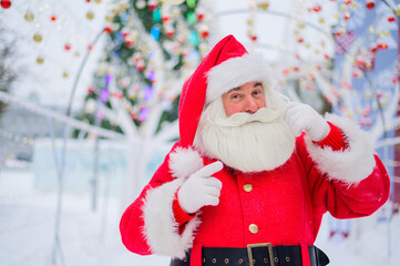 Portrait of an elderly man dressed as santa claus on the background of a christmas tree outdoors.