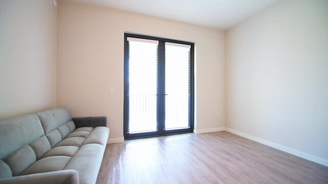 Pov point of view handheld walking shot of empty living room interior with futon couch gray grey sofa at new modern luxury apartment home house with balcony window doors by wooden laminate floor