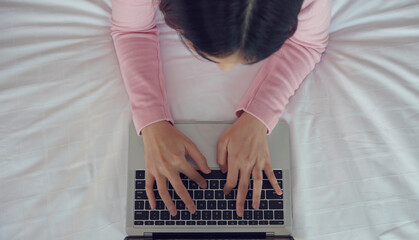 Hands of woman typing on laptop keyboard on bed.