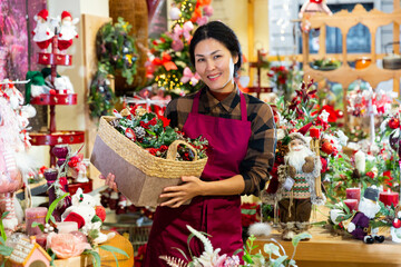 Asian woman home goods store worker in uniform standing in salesroom and holding christmas decorative item in hands.