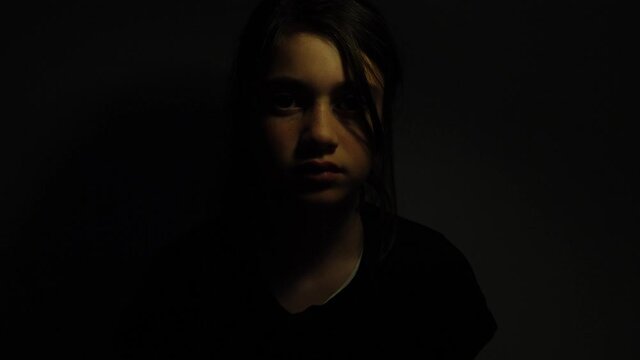 Upset girl (female age 11-12) emerging from the darkness.