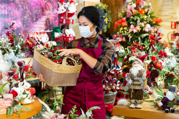 Asian saleswoman in face mask selling Christmas decorations at shop for decor