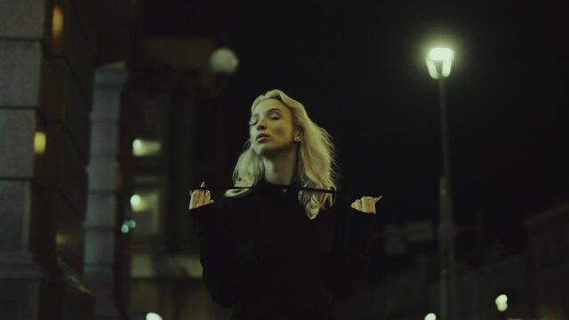 Blonde woman walking night alone in urban wear at modern city ights. 