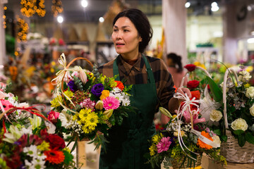 Fototapeta premium Portrait of a confident and successful Asian florist woman standing in a shop with flowers in her hands