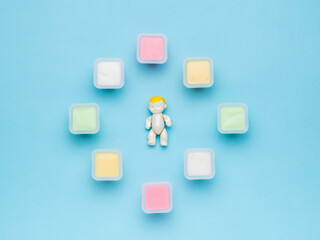 A baby figurine inside multicolored cups with multicolored yogurts. Natural healthy food. Flat lay.