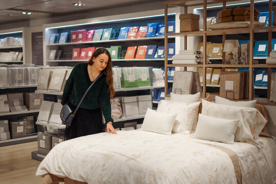 Cheerful woman choosing new bedding set in bed linen department, making purchases for new home