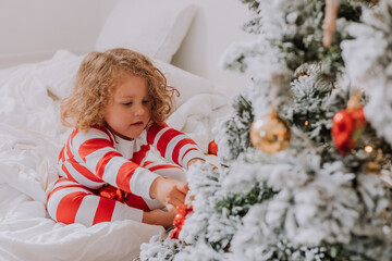 little girl in Christmas striped pajamas decorates the Christmas tree. lifestyle. High quality photo
