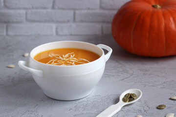 pumpkin soup with pumpkin seeds in a white bowl on a gray background