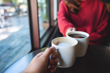 Closeup image of a man and a woman clinking coffee cups together in cafe