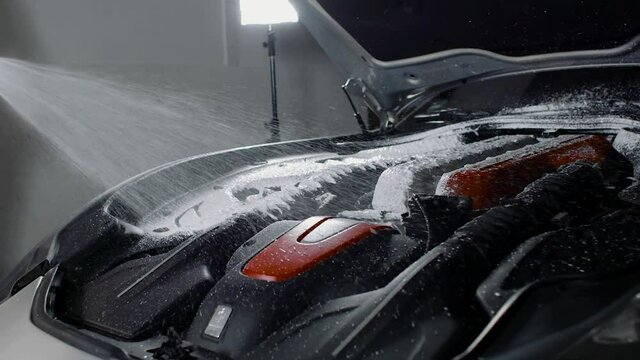 A dry engine bay getting foam soap being sprayed with high pressure washer on Ferrari engine bay. Whole engine in frame in slow motion.