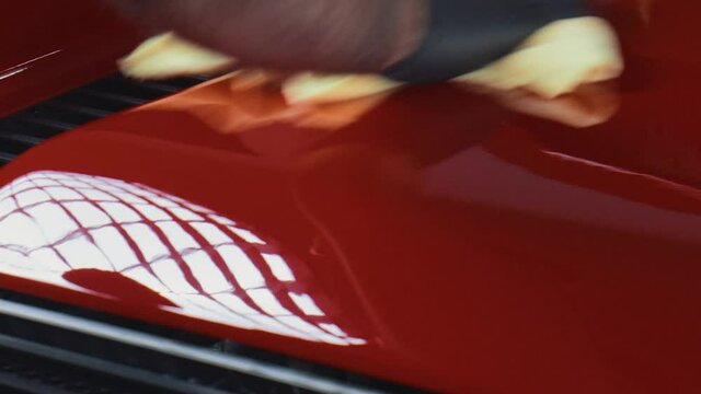 Wiping down red sportscar paint with microfiber cloth after polishing.
