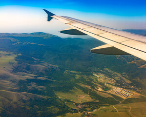 View of airplane wing, blue skies and green land during landing. Airplane window view.
